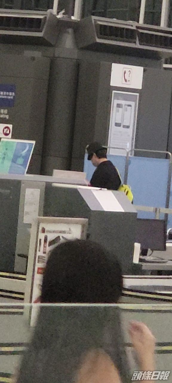 姜濤穿黑色大褸孭黃色背囊，現身機場。