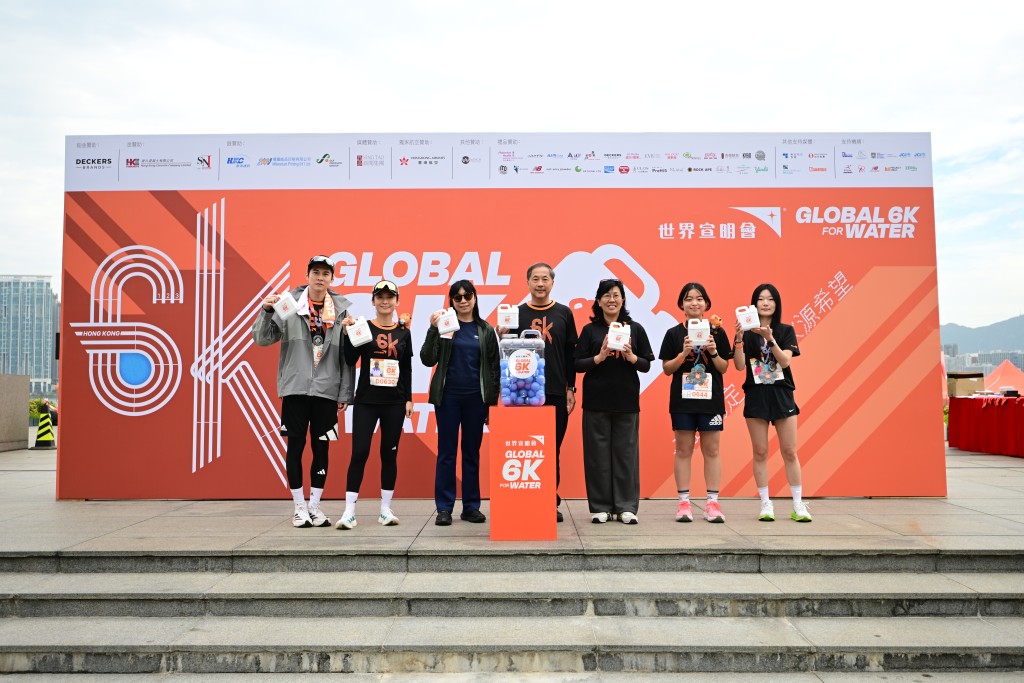 「Global 6K for Water」慈善跑開幕禮在早上 9 時開始，香港世界宣明會董事會主席陳朝光(左4)、世界宣明會總幹事馮丹媚(右3)、鉑金贊助 DeckersBrands 人力資源、社會責任及行政經理林盼(左3)、藝人周家怡 (左2)、陳家樂(左1)，以及韓國宣明會代表 Jiyun(右1)及 Jooha (右2)，一同將藍色膠波倒入水桶 之中，寓意貧困社區的孩子及家庭，在本會的水利項目協助下毋須再徒步走路 6 公里，便可輕易用水桶載滿清潔食水回家。圖片宣明會提供
