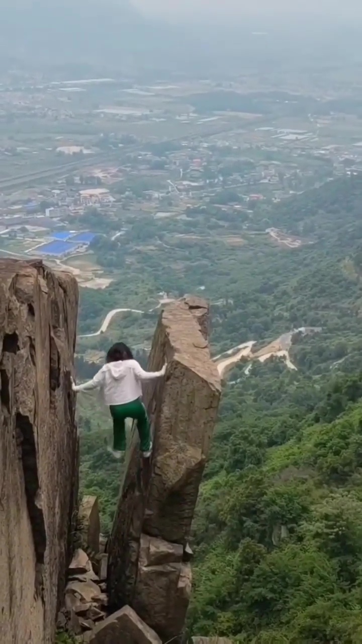 女子在懸崖與大石間的空隙攀爬。網上截圖