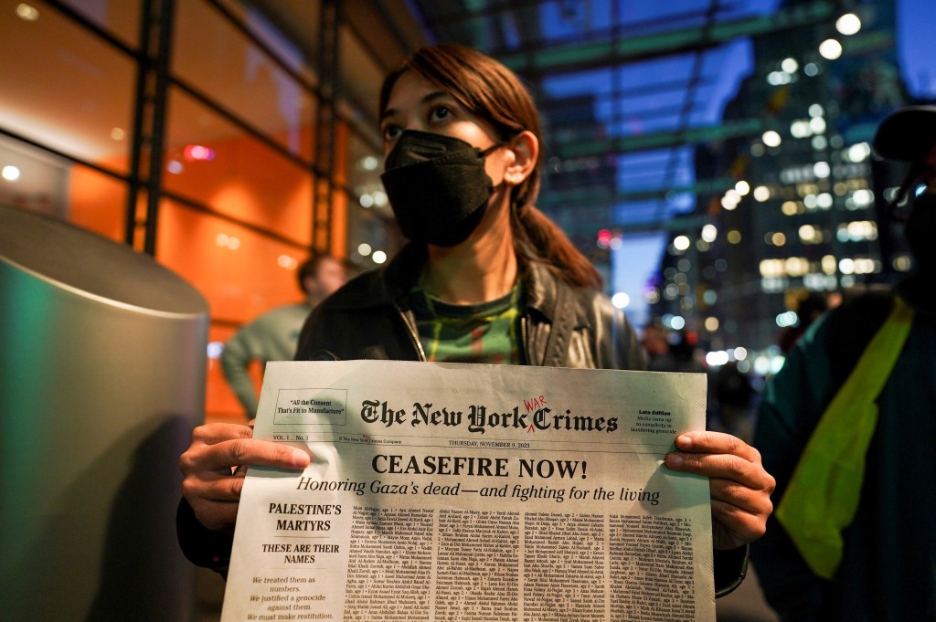 示威者高舉模仿紐時封面的紙張，上面的《紐約時報》被改成《紐約戰犯報》。路透社