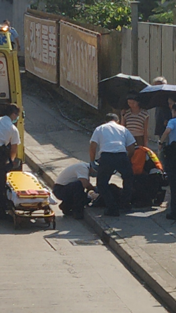 男童倒卧行人路,有街坊撐傘遮蔭。網上圖片 男童倒卧行人路,有街坊撐傘遮蔭。網上圖片