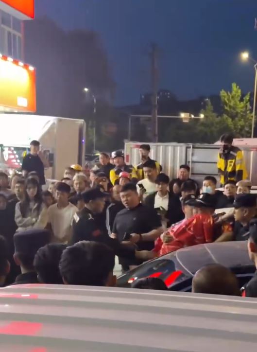 警員用身體為女事主遮擋身體，再用紅布裹身，護送她離開。影片截圖