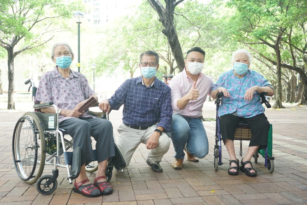 財政司司長陳茂波(左;深藍衫)一行與途人打招呼，並提醒他們記得申請消費券。