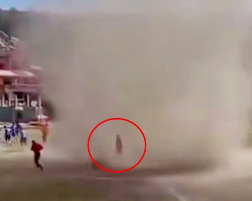 身穿红衣的球证，竟淡定地慢慢从「尘卷风」中走过。影片截图