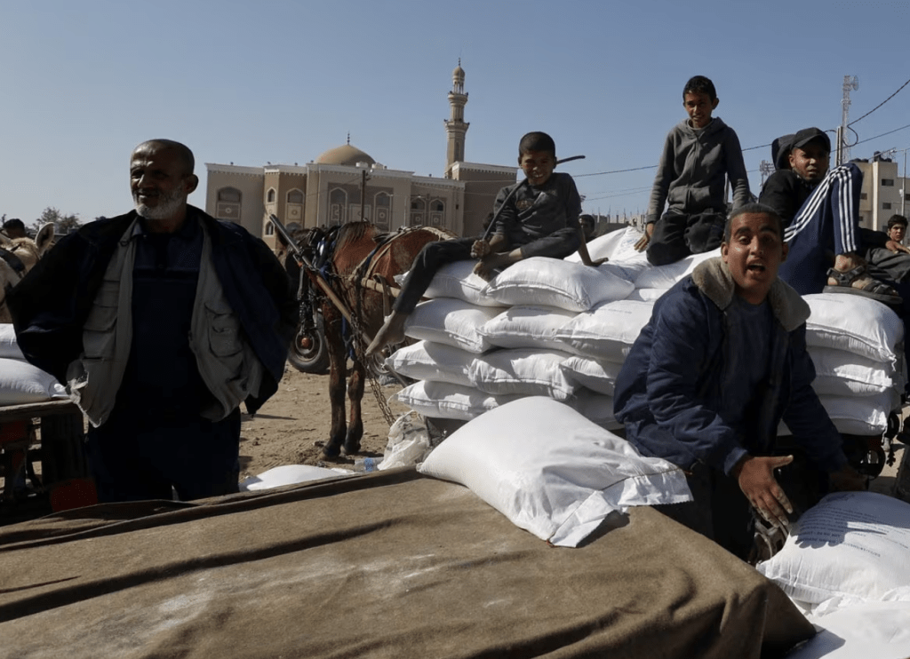 巴勒斯坦人聚集在一起接受近東救濟工程處分發的麵粉，孩子們坐在麵粉袋上。路透