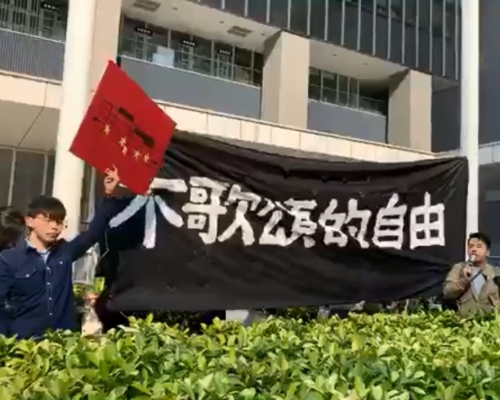 香港眾志成員早上爬上政總東翼前地的花槽掛起示威橫額。香港眾志facebook