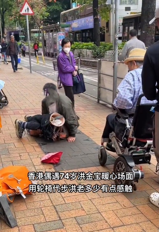 坐在轮椅上的洪金宝，因行人路窄加上修路，一名双残的乞丐用手撑起身体在洪金宝面前爬过。
