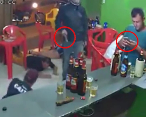 蒙面劫匪持槍威嚇,全部人都趴低,唯獨藍衣男在吧檯前專心用手機。(網圖)