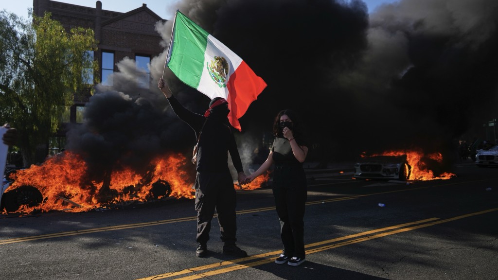 洛杉矶示威|示威者在一架烧成灰的Waymo的士旁高举墨西哥国旗。 美联社 洛杉矶示威|示威者在一架烧成灰的Waymo的士旁高举墨西哥国旗。 美联社