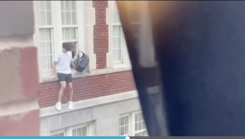 兩名年輕人將自己的物品從窗外傳遞出去，然後從窗台上跳到地上。