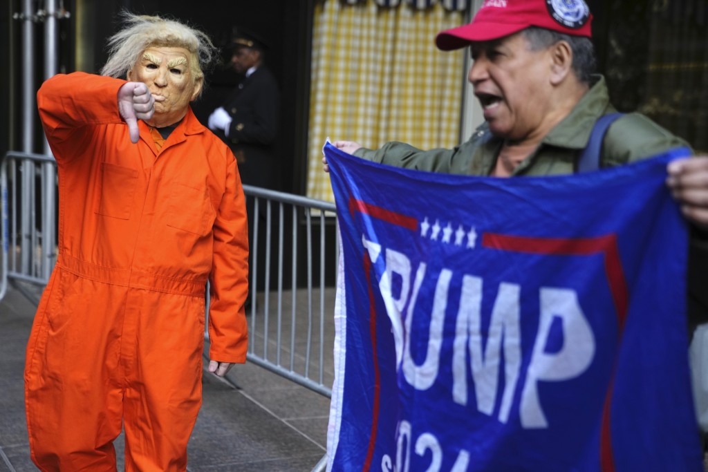 在纽约特朗普大厦外，一名男子（左）身穿囚服讽刺前总统特朗普，向特朗普支持者示威。AP