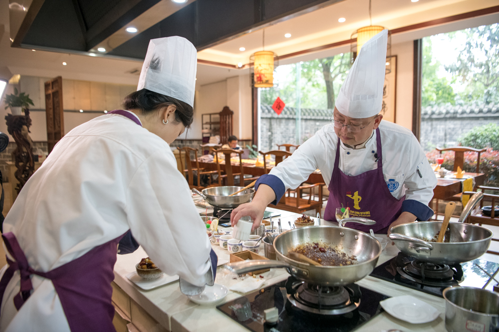 川菜博物馆副馆长张辉强（右）在教游客制作宫保鸡丁。 新华社
