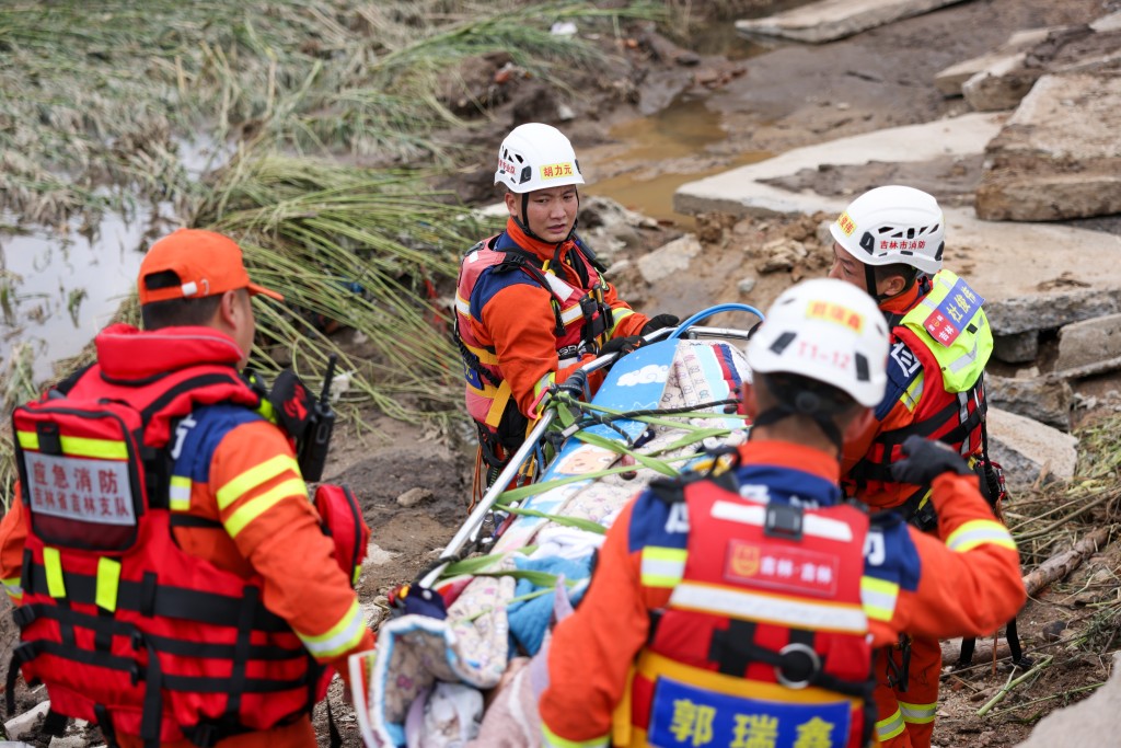  8月6日，吉林市消防救援支队队员用担架抬著曲凤霞通过损毁路面。新华社