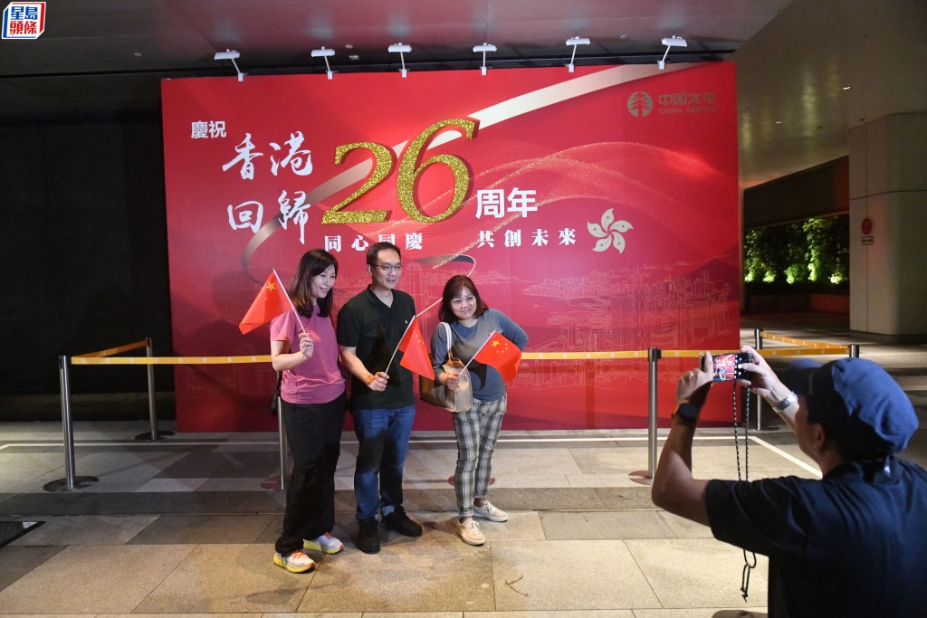 郭先生手执国旗在庆祝香港回归26周年广告牌前留影。陈极彰摄