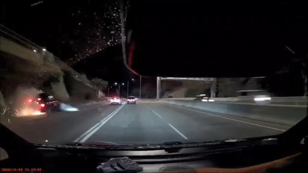 黑色私家車車身擦撞的士後失控撞向路旁石壆。網上片段截圖 黑色私家車車身擦撞的士後失控撞向路旁石壆。網上片段截圖