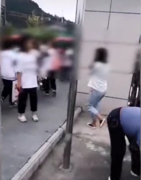 有女生在被迫卸妝後捂著臉進入校內。影片截圖