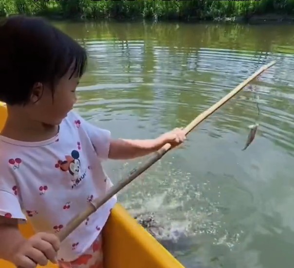 女童手持長桿伸入湖水要釣鱷魚。