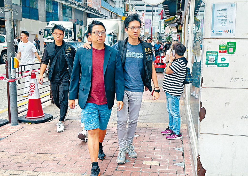 探員押解前油尖旺區議員朱江瑋,到旺角一間團購及網購店舖搜查。