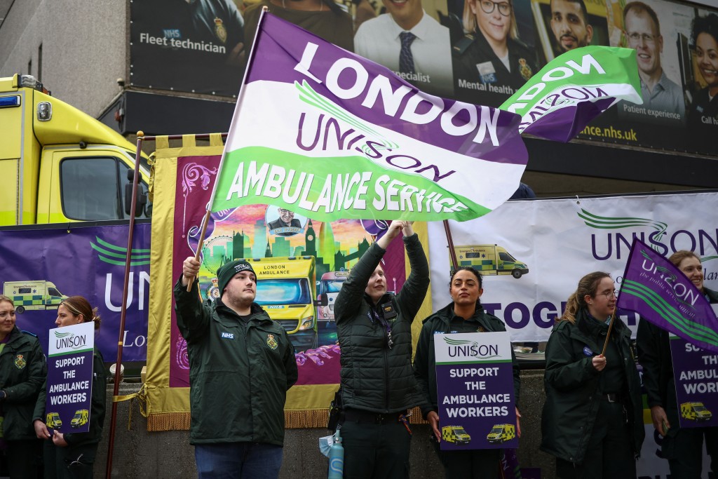 一名计划罢工的妇女在NHS伦敦救护车服务中心外举著Unison旗帜示威。路透社