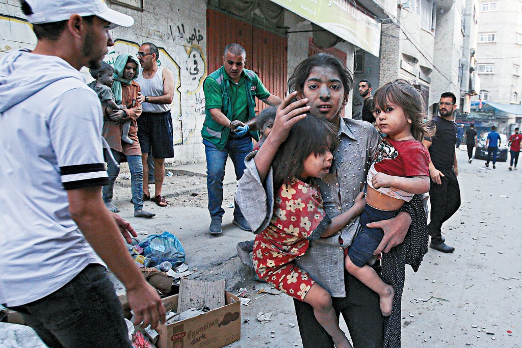 以軍空襲加沙城，巴勒斯坦婦女抱着兩童逃命。法新社