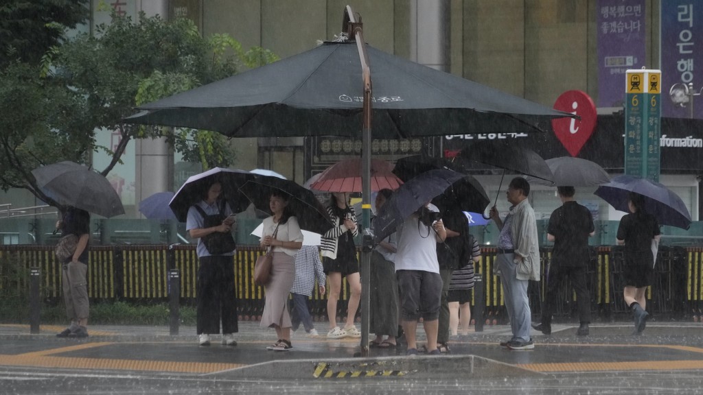 首尔民众撑伞也湿透，有人躲在帐篷下等过马路。 美联社
