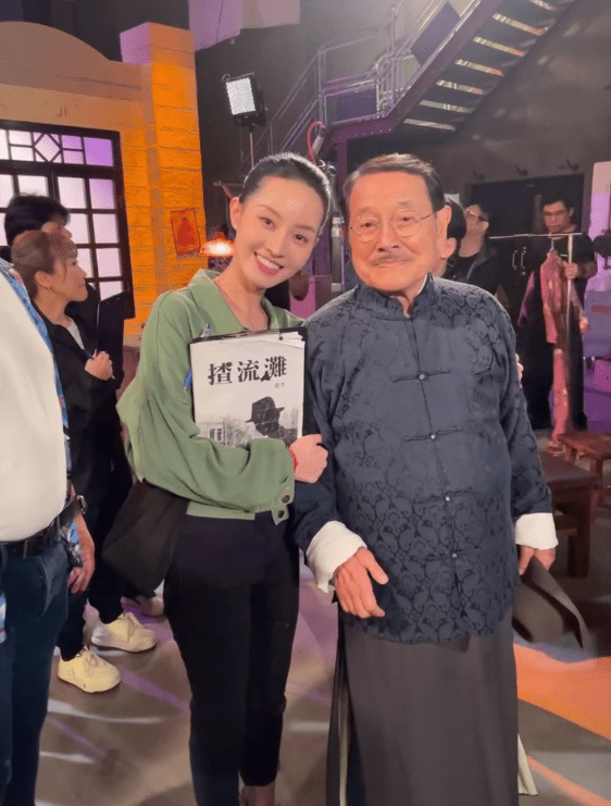洪曼芹在《愛回家》片場手持《揸流灘》劇本，與劉丹合照。