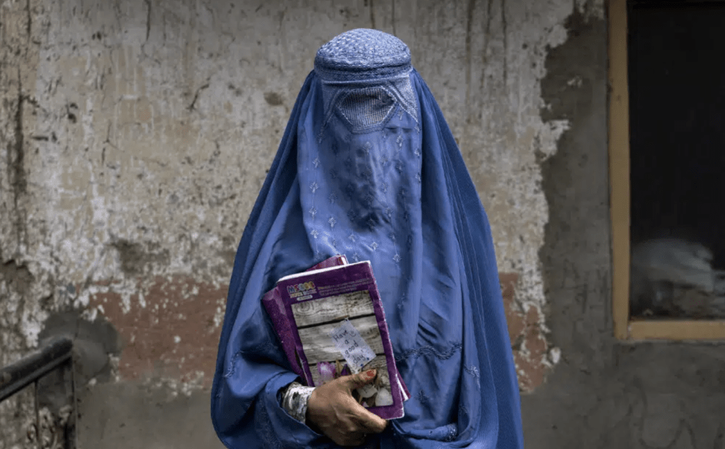 一名40岁阿富汗女子手持课本离开地下学校。AP