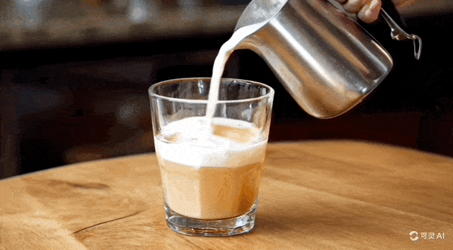 要求：一只手将牛奶从钢制打奶壶倒入桌上一杯咖啡中，背景为模糊的厨房。