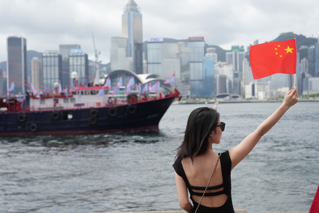 文化中心对出海面有渔船巡游，市民手持国旗打卡。