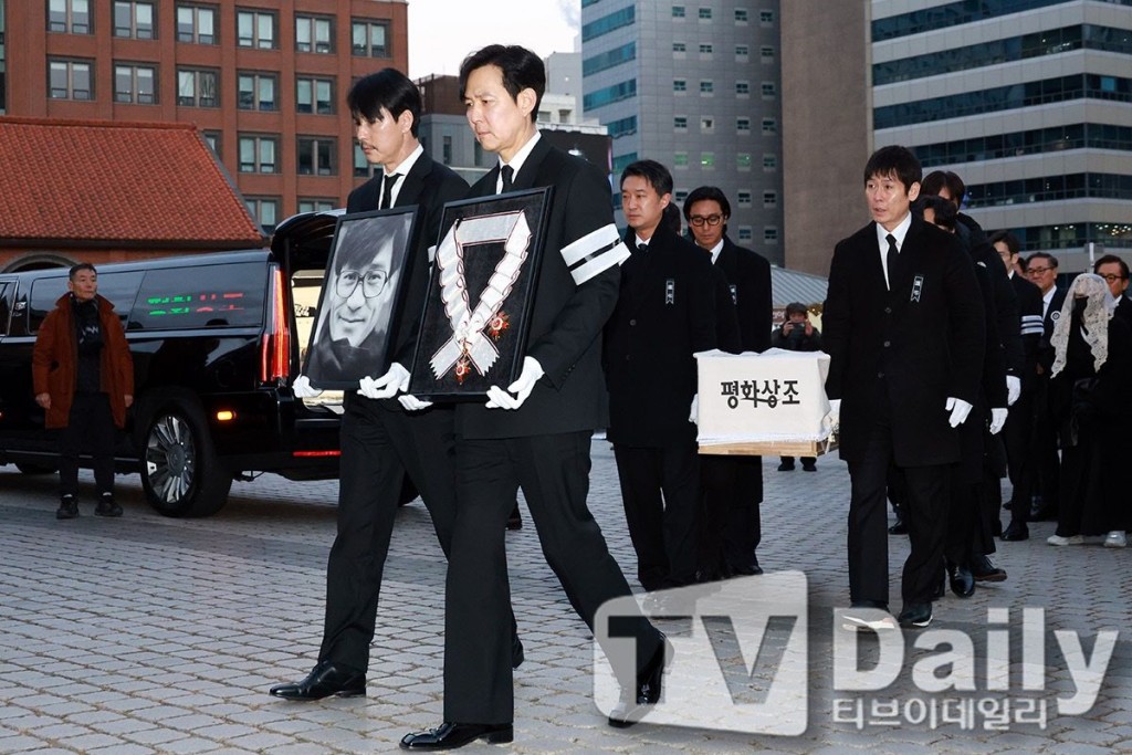 李政宰及鄭雨盛分別捧着安聖基獲追授的「金冠文化勳章」及遺照。