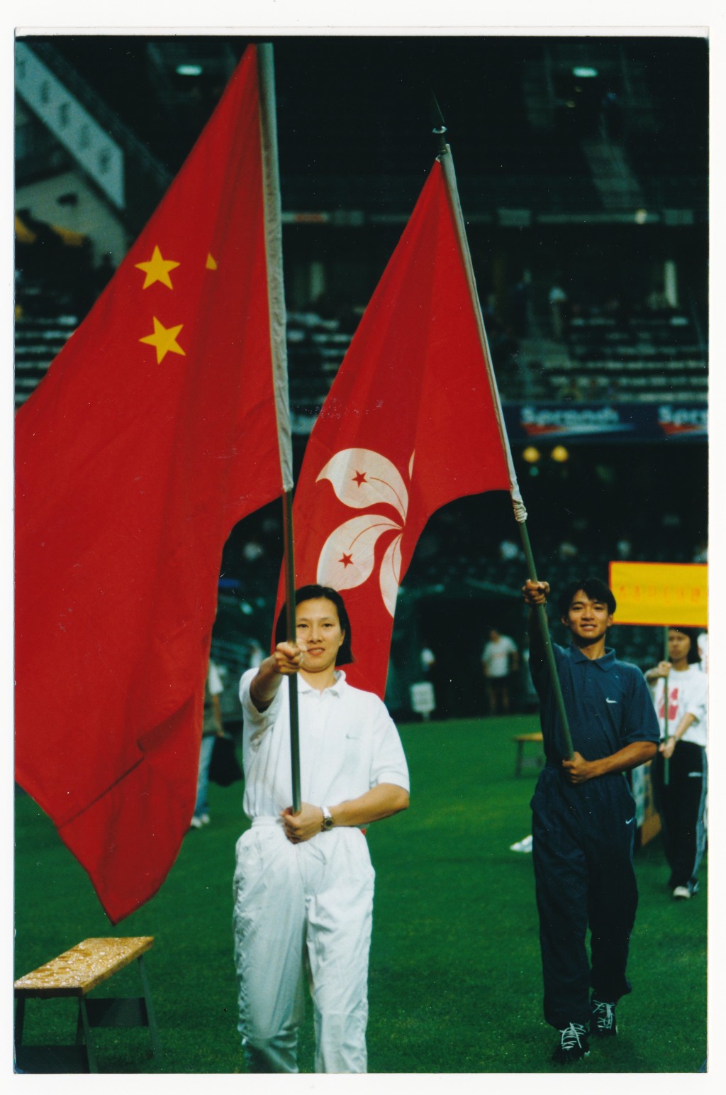 1997年7月李丽珊及单车手黄金宝手持中国国旗及特区区旗，在大球场回归杯赛前引领56支体运队伍健儿，绕场一周。