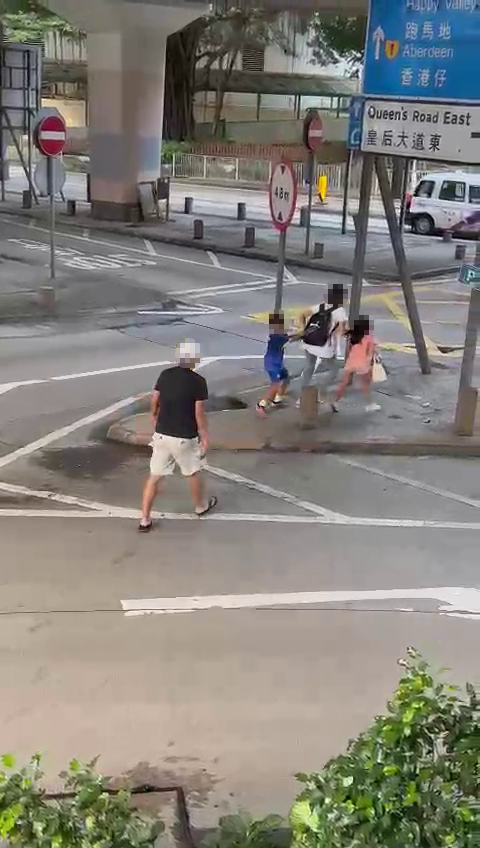 一名短发女子拖住两名小童横过马路。
