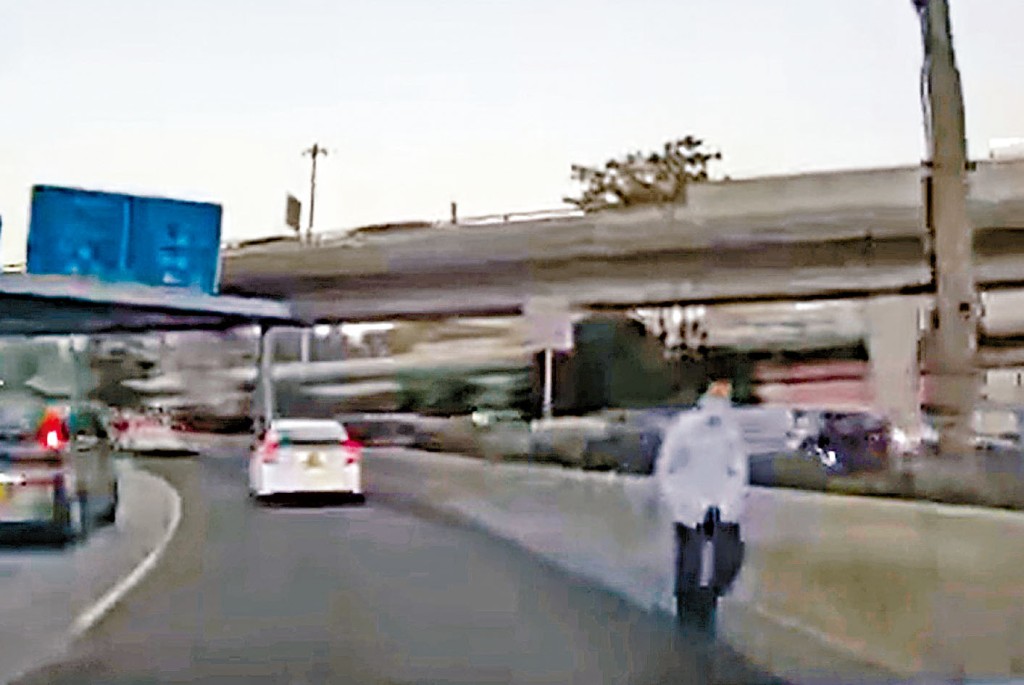 老翁在公路上行走不時有車輛在其身旁駛過。