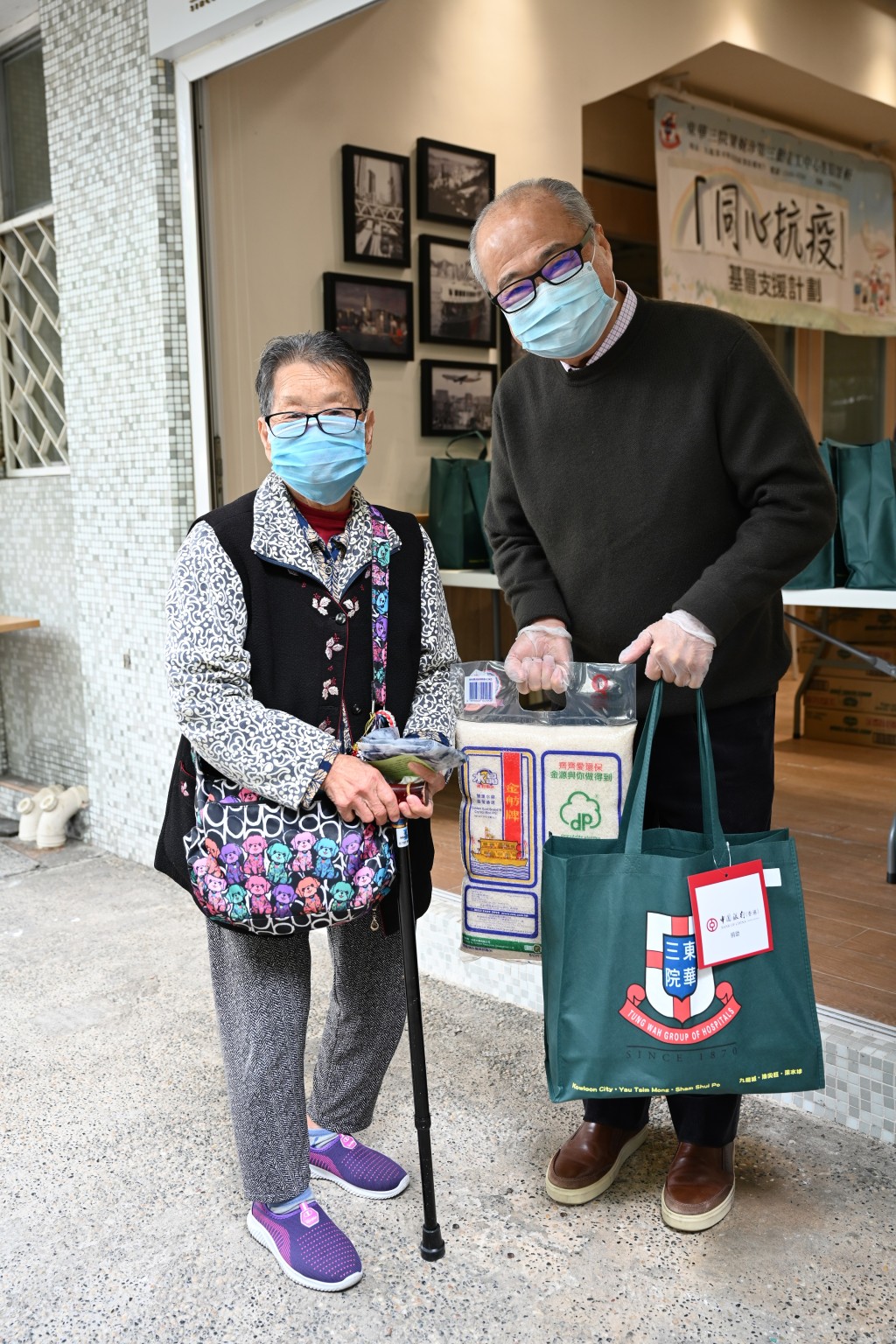 周松崗(右)聯同東華三院的代表,在深水埗白田邨向長者派發口罩等抗疫物資。 政府圖片