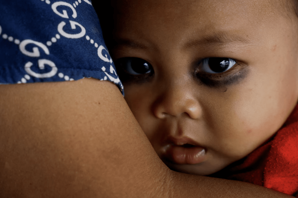 2024 年3 月15 日，印尼萬丹省直落漁村，一名眼睛塗著眼影的9 個月大嬰兒望着垃圾堆。路透社