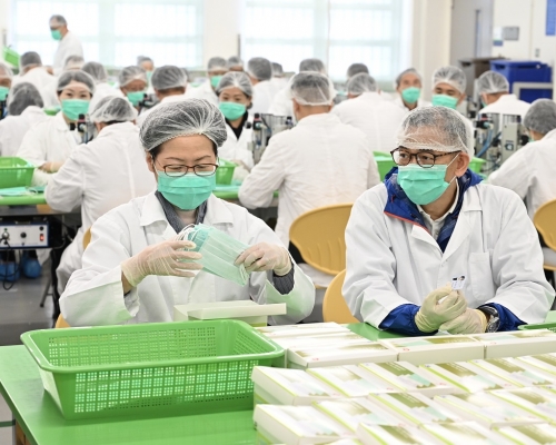 林鄭月娥(左)參與包裝口罩的工作。旁為懲教署署長胡英明。新聞處圖片