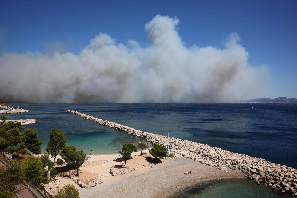 法国南部马赛郊区科比埃海滩,背景中弥漫着山火产生的浓烟。 法新社 法国南部马赛郊区科比埃海滩,背景中弥漫着山火产生的浓烟。 法新社