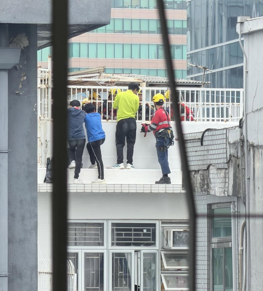 3名青年站在天台，雙手扶着欄邊，身旁有消防高空拯救專隊人員協助。網上圖片