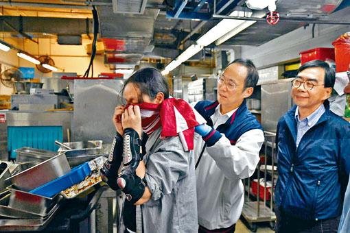 ■卫炳江（中）在厨房了解现况时，细心为留守者绑实美国旗口罩。