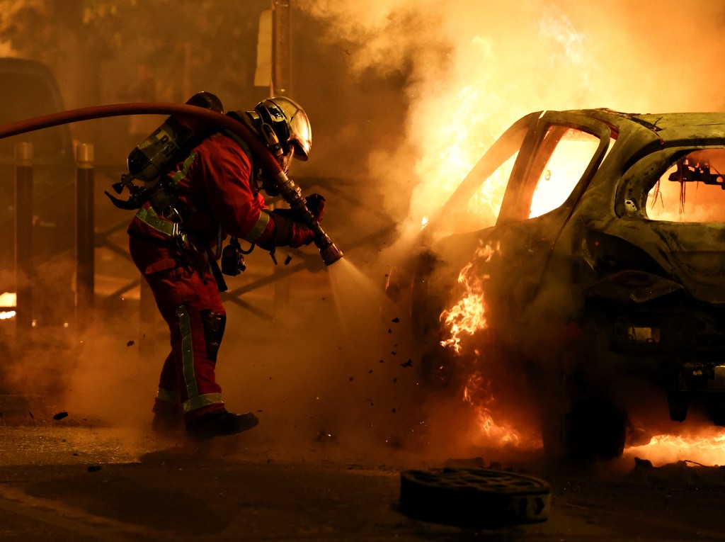 骚扰中，一辆汽车被烧毁，当地消防员正在救火。路透社