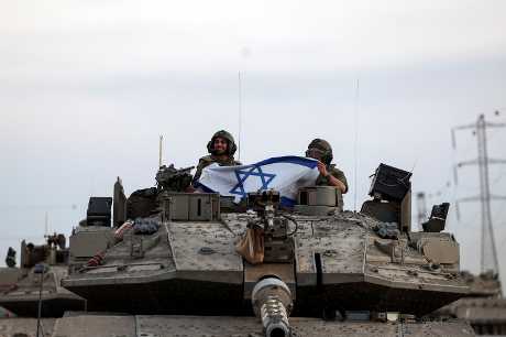 在以色列靠近加沙的边境附近一辆坦克上的士兵举著以色列国旗。路透社