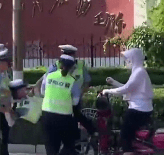 女輔警準備用腳踢騎電動單車的女子，被同事們拉開。