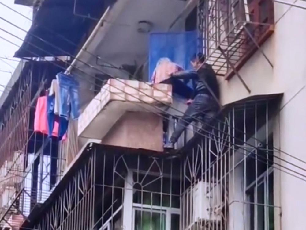 工人將老婦抱住，助爬回陽台。影片截圖
