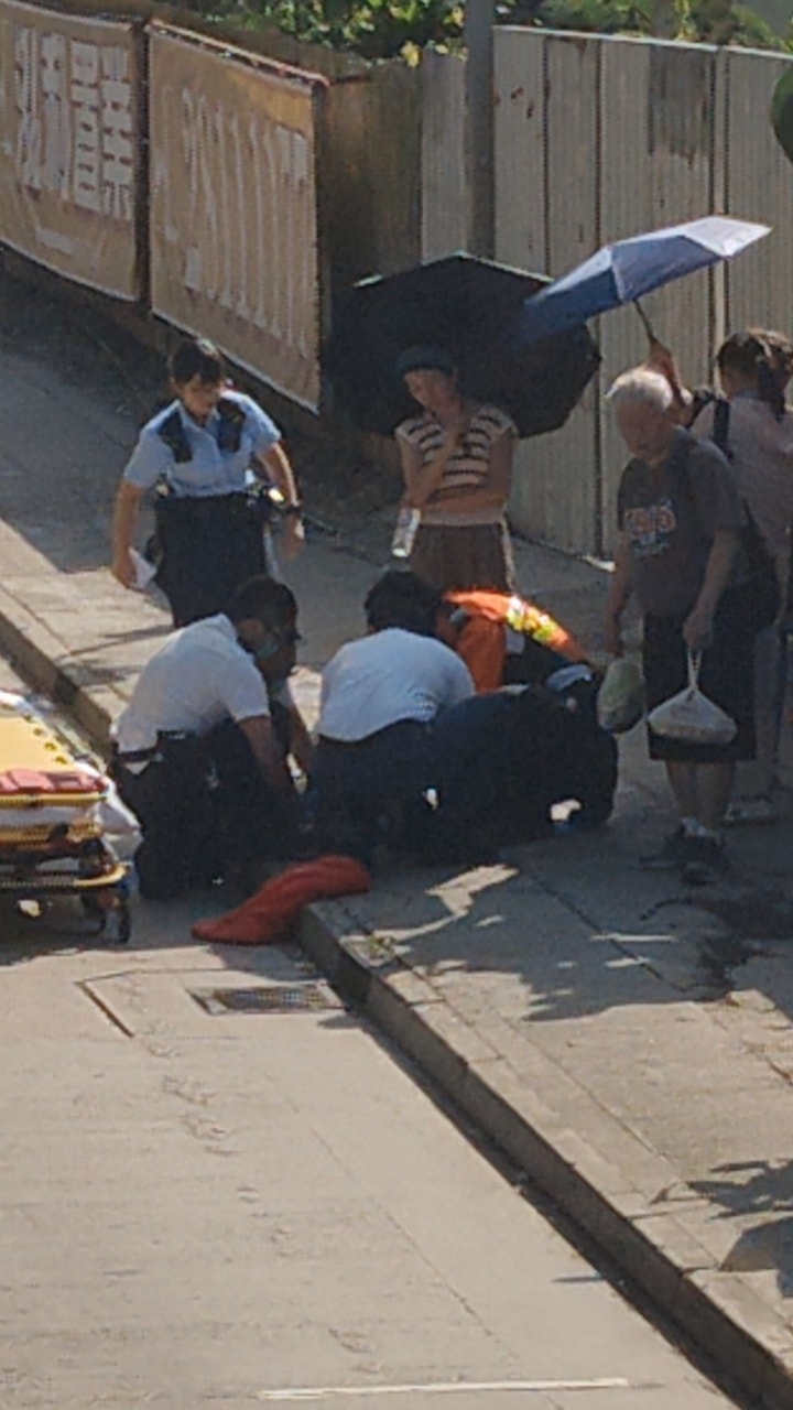男童倒卧行人路,有街坊撐傘遮蔭。網上圖片 男童倒卧行人路,有街坊撐傘遮蔭。網上圖片