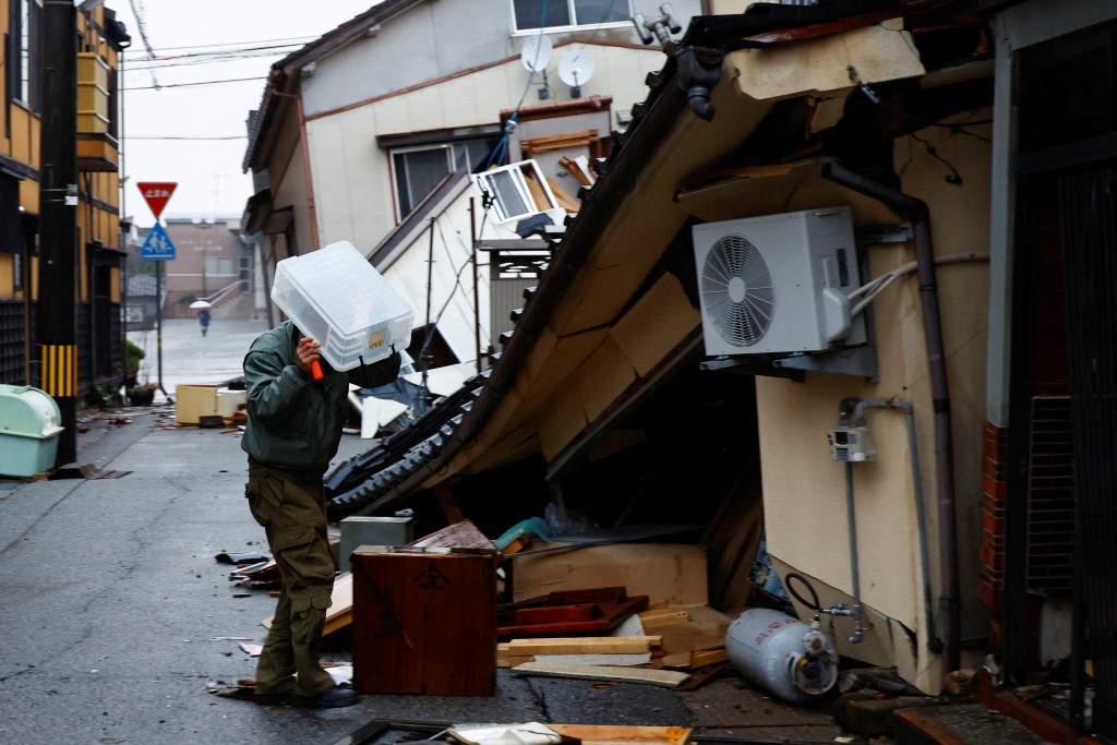 日本石川縣輪島，一名男子在雨中用塑膠盒蓋住自己，準備收拾行李，然後前往另一個城市。路透社