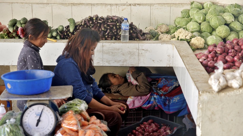 在不丹首都廷布，一个女孩在母孩准备菜档营业时玩手机。 路透社