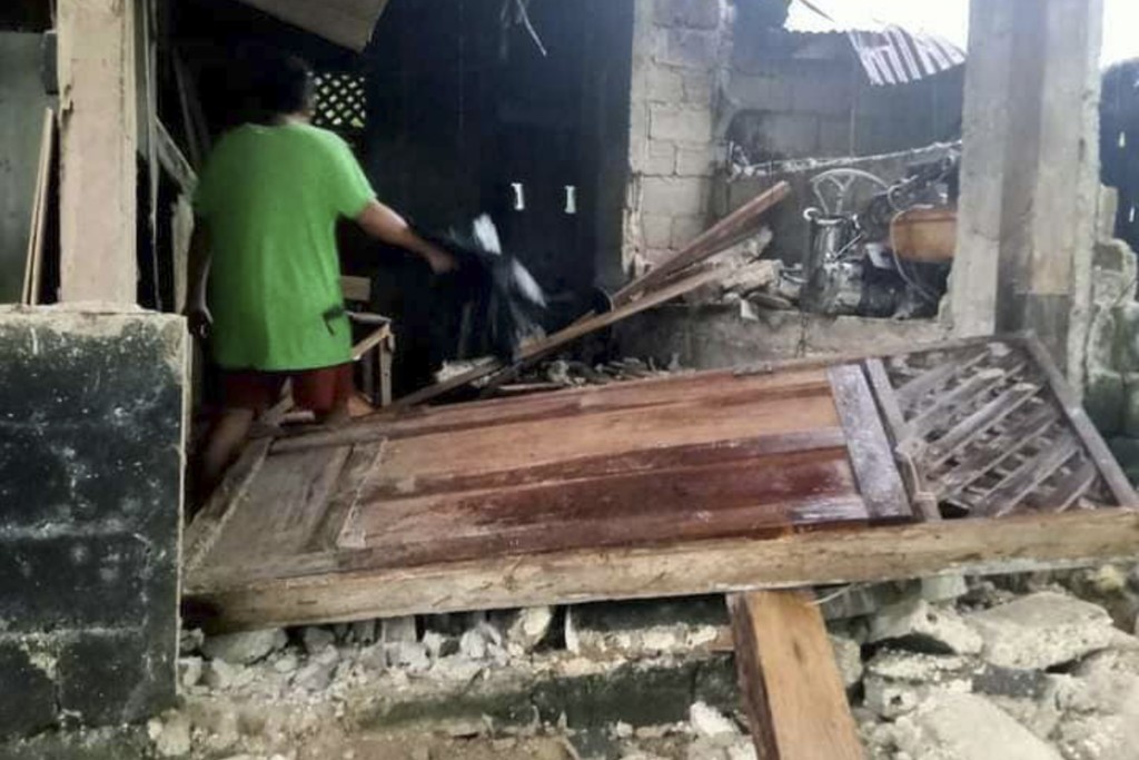 菲律賓南部蘇里高省海納圖安鎮發生地震後，一名村民在受損的房屋旁行走。AP