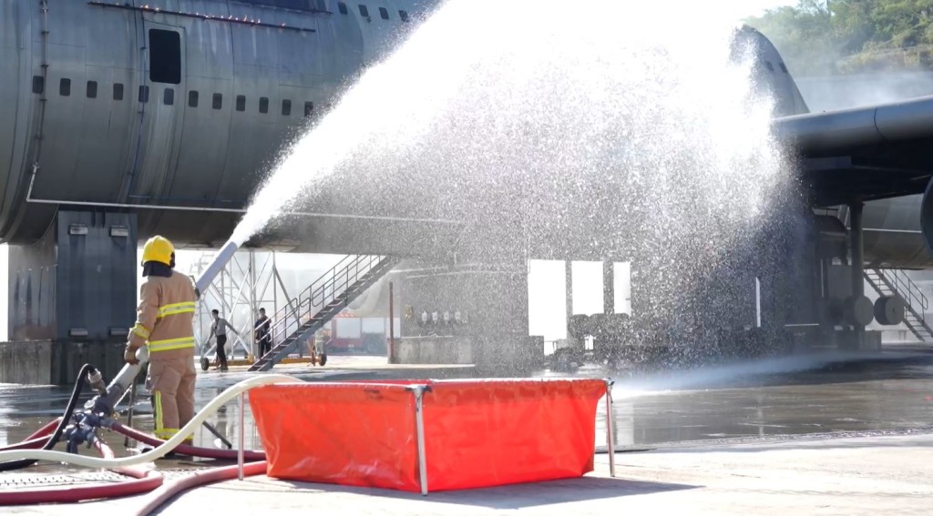 在模拟飞机事故训练场内，消防员接受救火训练。影片截图