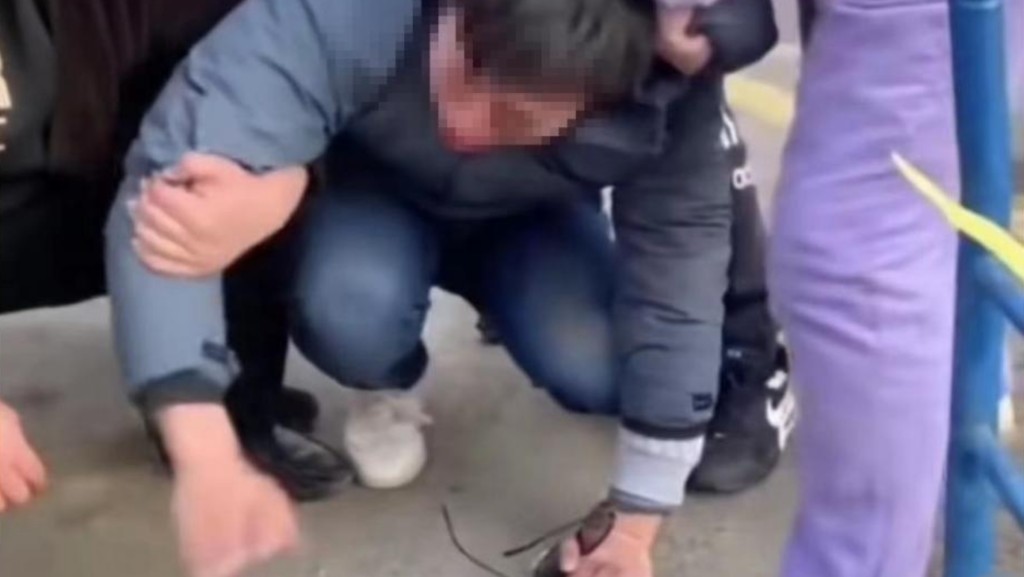 一男子被多人钳住手臂跪在地上。影片截图