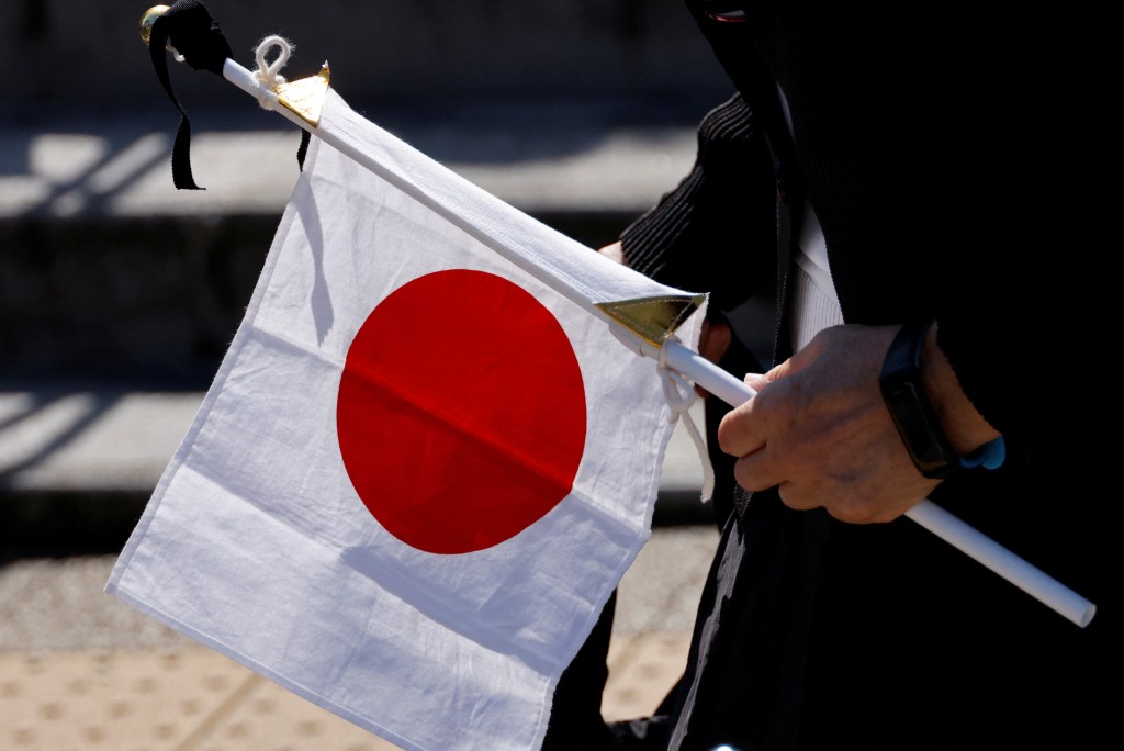 一名民眾舉著帶有黑絲帶的日本國旗表達敬意。路透